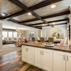 an open concept kitchen and living room with wood flooring, white cabinets and wooden beams