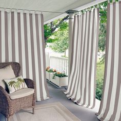 a chair sitting on top of a porch next to a window covered in white and gray striped curtains