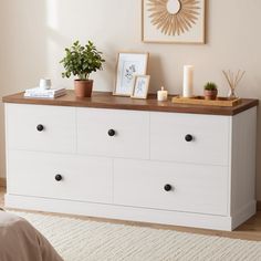 a white dresser with some plants and pictures on it