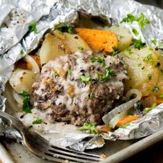 some food that is sitting in foil on a plate with a fork and spoon next to it