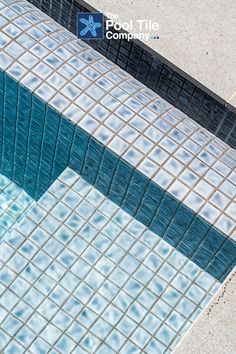 a blue and white tiled swimming pool next to a concrete wall with the words pool tile company on it