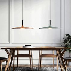 a dining room table with chairs and two pendant lights hanging over it, in front of a white paneled wall