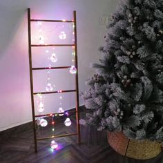 a small christmas tree next to a ladder in a room with lights on the wall