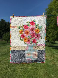 a quilt hanging on a clothes line with flowers in a vase painted on the front