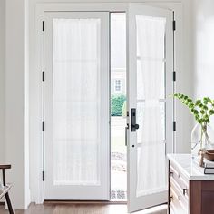 an open white door with sheer curtains on the outside and inside, in front of a wooden dresser