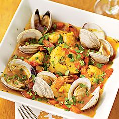 a white plate topped with clams next to a glass of wine and silverware