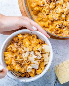 two hands holding a bowl of macaroni and cheese