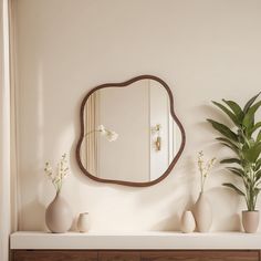 there is a mirror on the wall above some vases with flowers and plants in them