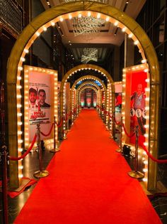 a red carpeted hallway with lights and posters on the walls, leading to an entrance