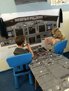 two children sitting at a table in front of an airplane control panel with buttons on it