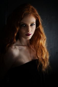 a woman with long red hair is posing for a photo in a black dress and dark background