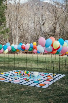 a bunch of balloons are in the air on a picnic table with plates and cups