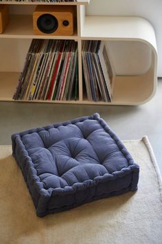 a blue dog bed sitting on top of a rug in front of a book shelf