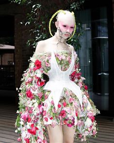 a mannequin with flowers on it's body and hair in front of a building