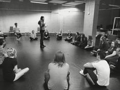 a group of people sitting on the floor in front of a man speaking to them