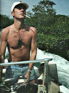 a man with no shirt on riding in a boat next to a waterfall and trees