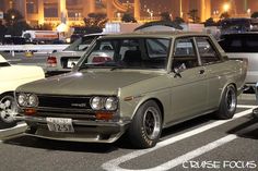 an old car is parked in a parking lot with other cars and buildings in the background