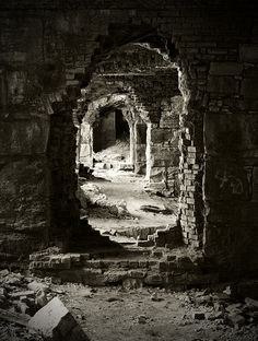 black and white photograph of an old building with stone walls, doorways and pillars