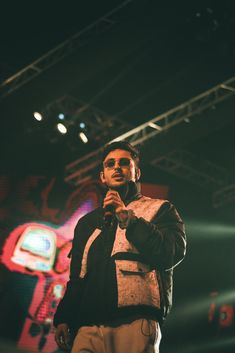 a man standing in front of a microphone on top of a stage with lights behind him