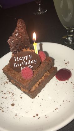 a piece of chocolate cake with a lit candle on it sitting on a white plate