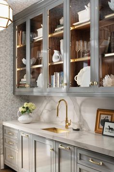 a kitchen with gray cabinets and white marble counter tops, gold faucet handles