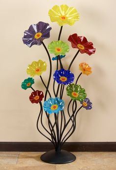 multicolored glass flowers are arranged on a black metal stand in front of a beige wall