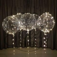 three clear balloons with lights on them sitting in front of a black curtain and drapes