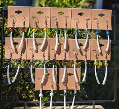 several pairs of earrings hang from hooks on a wall outside in front of trees and bushes