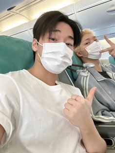 two people sitting on an airplane wearing masks and giving the thumbs up sign with their hands