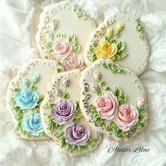 four decorated cookies with flowers on them sitting on a white lace tablecloth, ready to be eaten