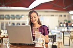 a woman sitting at a table with a laptop and cell phone in front of her