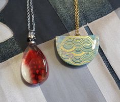 two necklaces with different designs on them sitting on a tableclothed surface, one is red and the other is green