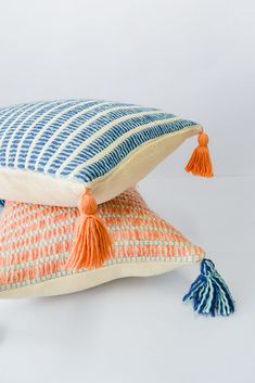 two pillows with tassels on them sitting next to each other, one is orange and the other blue