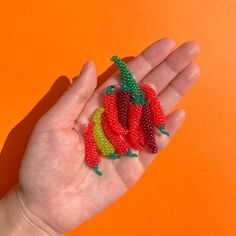 a hand is holding some beads in the shape of strawberries on an orange background