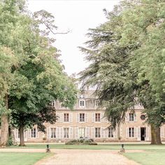 a large building with trees surrounding it and people walking around the grounds in front of it