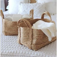 three woven bags sitting on top of a bed next to pillows and blankets, with one bag in the middle