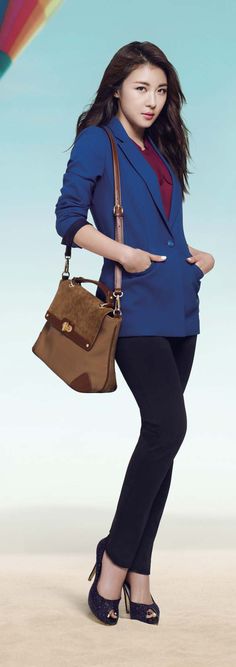 a woman holding a brown purse standing in front of a rainbow colored kite with her hand on her hip