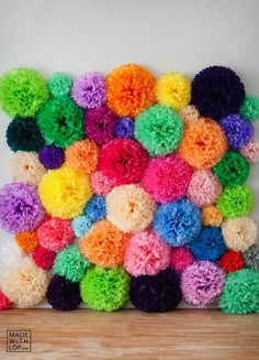 multicolored fluffy pom poms are arranged on a white wall in front of a wooden floor