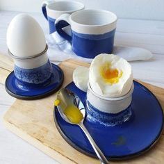 an egg is sitting on a blue plate next to two cups