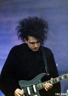 a man with curly hair playing an electric guitar on stage at a concert or festival