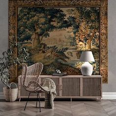 a room with a large tapestry on the wall next to a wicker chair and sideboard