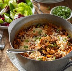 a pot filled with food sitting on top of a wooden table next to plates of salad