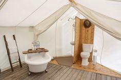 a bathroom with a tub, toilet and sink inside of a tented area that has wood flooring