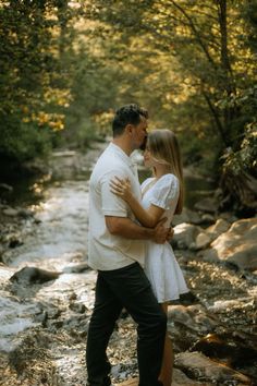 a man and woman standing next to each other in front of a river with rocks