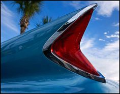 the tail end of a blue car with a palm tree in the backgroud