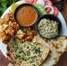 a white plate topped with different types of food on top of a wooden table next to vegetables and sauces