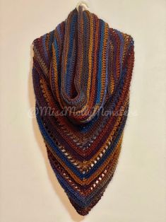 a multicolored crocheted shawl hanging on a wall with white background