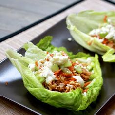 two lettuce cups filled with shredded meat and vegetables on a black plate next to a fork