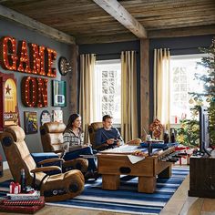 two people sitting in a living room with christmas decorations on the walls and a tree