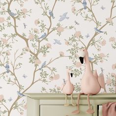 two pink flamingos standing on top of a dresser next to a wallpapered tree